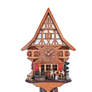 8-Day Black Forest Chalet coocoo clock. The half-timbered cuckoo clock has darker wood in the lower part of the clock and lighter stucco on the upper half. The dial is dark brown. A dachshund sits on the left corner of the clock, beside a pile of wood. Flower boxes decorate a fenced-in water fountain. Two beer drinkers sit on a table underneath windows with red shutters. Next to the dial are two turrets with open red window shutters. The steep roof matches the Tudor-style house.