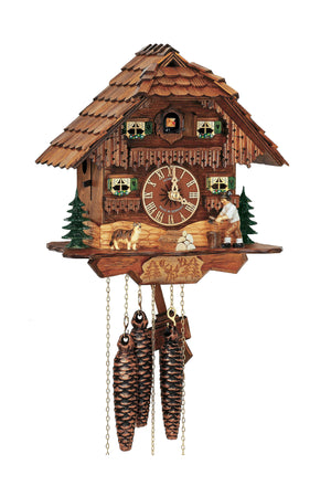1-Day Schneider Chalet Coocoo clock without music. There is an evergreen tree and a man chopping wood on the right, a pile of logs in the middle and a German Shepherd on the left. There are two windows with green shutters and flower boxes underneath next to the dial in the middle. Above the balcony there are two more windows with green shutters and flowers on either side of the coockoo who comes out behind the door. 