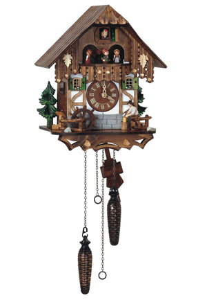 Quartz Schneider half-timbered chalet coocoo clock. A green fir tree with a water trough and spinning water wheel sit on the left side of the clock. A woodchopper works on the right. There are green trees on both sides. The front looks like grey stones at the bottom and half-timbered wood with  white stucco. The top half is dark wood. Two windows beside the dial have green shutters and flower window boxes. Dancers are spinning on the balcony above. The cuckoo comes out behind his door at the very top.