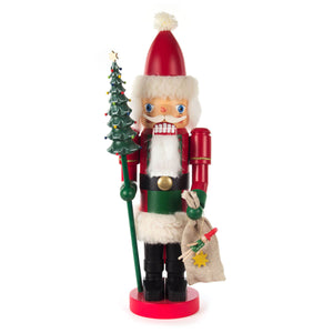 This Dregeno Nutcracker - Santa with Tree Glazed is a festive addition to any holiday décor. Crafted from wood, it features a standing Santa figure dressed in a traditional red suit, holding a small Christmas tree in one hand and a burlap sack full of gifts in the other. Add a touch of Christmas cheer to your home with this delightful decoration.