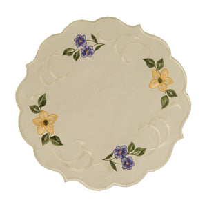 Round white table linen with scalloped edges, and a border of yellow and purple spring flowers and a swirling white stitched design between them.