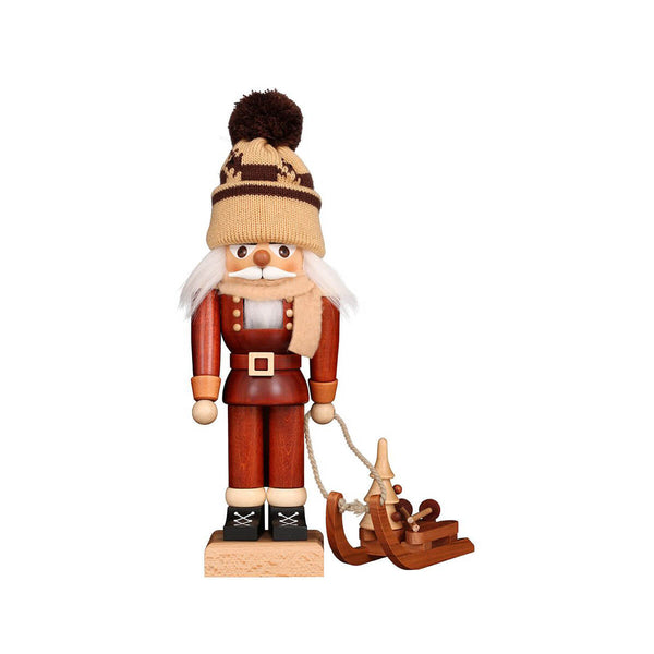 Handcrafted winter nutcracker with a pom-pom hat, scarf, and wooden sled carrying a small fir tree and wooden poles, capturing the joy of a snowy adventure