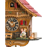 Discover the allure of this Chalet-style Cuckoo Clock, featuring a romantic kissing couple. Vibrant red accents on the roof, door, and shutters add charm. Small details like a little orange cat, a milk jug and a traditional water trough add to the clock’s charm.