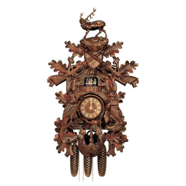 8-Day Traditional Black Forest Hunter coocoo clock. The solid wood traditional style clock features a rabbit on his hind legs on the right edge of the clock and a pheasant looking up on the left edge. The front is decorated with oak leaves. A hunter’s pouch is featured at the bottom. A horn encircles the dial. Dancers spin on a balcony underneath the cuckoo bird. The roaring stag stands above the crossed rifles at the top of the clock. 