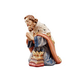 This figurine portrays Caspar, one of the three Magi, kneeling in reverence before the Infant Jesus. Dressed in regal attire of red cloak, blue robe, and ermine stole, Caspar's full beard adds to his majestic appearance. His hands are folded in reverence, and a golden crown and a gift of gold adorn his side.