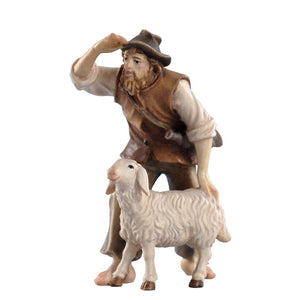 Pema Kostner Nativity shepherd with a dark grey hat and a brown vest, wearing grey pants and a white shirt, gazes into the distance while gently touching his sheep. A horn slings over his shoulde