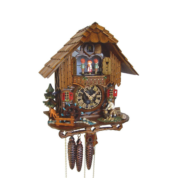 1-Day Schneider Black Forest Chalet Coocoo clock with music. A man is chopping wood on the right side of the platform. On the left, a water wheel spins, and a little brook lined with pebbles on each side is flowing across. There is an evergreen tree and a grazing deer on the left. The clear faced dial shows the sophisticated mechanical movement inside the clock box. Dancers spin on the balcony, above it is the cuckoo clock door underneath the roof with wooden shingles.
