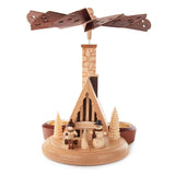 This beautiful, hand carved Christmas pyramid holds a candle on each of the sides of its base to provide gentle lighting on every side when in use. The heat from the candles causes the center of the pyramid to turn, displaying every side of the center design as it rotates. This pyramid features a single tier design with a ski hut – Skihuette and a large chimney. There are several carved trees in natural wood tones, a happy snowman and child dressed for winter fun in front of the hut.