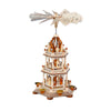 A 3-tier wooden Christmas pyramid featuring the Holy Family on the bottom tier, a shepherd with sheep on the middle tier, and angels with trumpets on the top tier, spinning gently with candlelight.