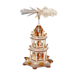 A 3-tier wooden Christmas pyramid featuring the Holy Family on the bottom tier, a shepherd with sheep on the middle tier, and angels with trumpets on the top tier, spinning gently with candlelight.