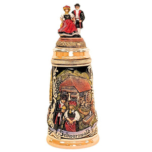 The front displays a scenic black-forest architecture and a colorful couple in traditional dress at the front of the display as well as atop the lid.
