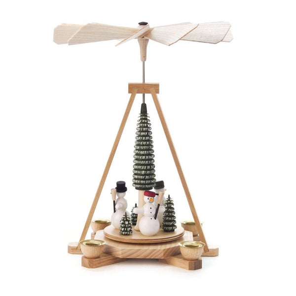 This beautiful, single tier Christmas pyramid holds a candle on each of the sides of its base. In the center, a carved, green Christmas tree stands as snowmen, wearing colorful winter hats and holding straw brooms, stand at every side of the center platform around the tree, with small evergreen trees in front of them.