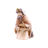 Sculpted wooden Kneeling King figurine for Artis Nativity set. He wears a white robe, with a tan cloak, and a turban hat, as he holds a wooden box.