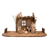 Sculpted wooden Artis Nativity starter set. Includes a wooden stable and display base, with figurines of the Holy Family, Angel, Ox, and Donkey.