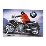Vintage metal advertising sign of a cyclist dressed in red on a BMW K100 RS motorcycle, driving through the mountains.