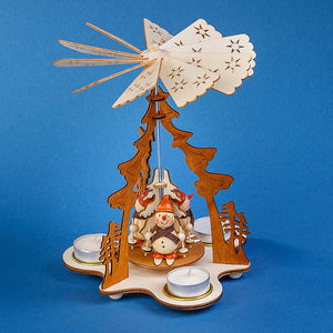 The natural-colored Pfaff Christmas pyramid is made out of wood and works with four tealight candles. The one-tier pyramid is 9 inches tall and shows four smiling snowmen on skis. They are wearing hats and scarves and are holding poles. The laser cut details include a light-colored sectioned tree at the center and a 4-piece dark-colored arch above.