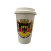 White ceramic coffee mug with a rubber lid, with a German Eagle and flag crest in the center. A tower rests atop the crest and a curling banner of red and yellow on the sides. Below, it reads "Deutschland" and "Germany."
