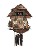 1-Day Schneider Chalet Coocoo clock with music with a man chopping wood on the right, a water wheel on the left and an evergreen tree with a bench next to it. The house is half white stucco / half timber on the lower half. There are two windows with green shutters and flower boxes next to the dial. The upper half is made with dark stained wood. The dancers dance on the wide balcony, flanked by green shutters and the cuckoo comes out behind the door under the shingled roof.