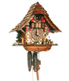 1-Day Schneider Chalet Coocoo clock with a man chopping wood next to a pile of logs on the right and a goose on the left. A water trough, wooden fountain with evergreen and stones are on the left side of the house. The half-timbered house is white stucco with a rounded timber structure. Next to the dial in the middle there are windows with red shutters and flower window boxes. Above sits a balcony and the cuckoo door is also flanked by a set of red shutters. The curved roof is made out of wooden shingles.