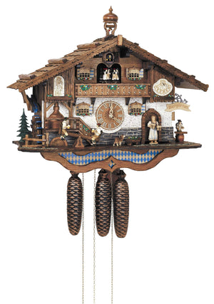8-Day Schneider Black Forest Coocoo clock with music. The Bavarian beer garden themed clock is white on the lower level. A waitress carrying several beer mugs comes out the door, a guest is sitting at a table under the Biergarten sign at the right. Two men hold their beer steins on a teeter-totter on the left, decorated by a water wheel and two evergreen trees. The dark stained and ornately carved wooden balcony on the top shows the dancers, the cuckoo bird above them. A bell tower sits on the roof. 