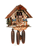 8-Day Schneider Black Forest Chalet Coocoo Clock with music. The half-timbered chalet is white with tan and brown accents. A beer drinker sits at a table, a water pump and trough and tree decorate the right corner. A bench sits directly underneath the dial and a waterwheel with a stone wall and two large green fir trees are on the left. The balcony on the top shows the spinning dancers, the cuckoo comes out above them. The roof is made out of shingles.