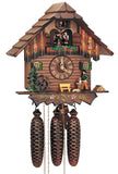 8-Day Black Forest Chalet coocoo clock with music. The base of the dark wood house is decorated with painted flowers. A green tree grows next to the water wheel on the left, a light-colored bench sits in the middle and a wood chopper chops wood next to a pile of logs. The windows on the rustic log front have green shutters and floral boxes. The dancers spin above the balcony also decorated with flower boxes. The roof has shingles.