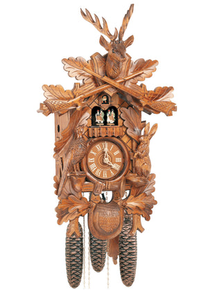 8-Day Black Forest Traditional coocoo clock. The solid wood traditional hunter style clock features a rabbit on his hind legs on the right edge of the clock and a pheasant looking up on the left edge. The front is decorated with oak leaves. A hunter’s pouch is featured at the bottom. The dial is encircled by a horn. Dancers spin on a balcony underneath the cuckoo bird. The stag head with large antlers sits above crossed rifles at the top of the clock.