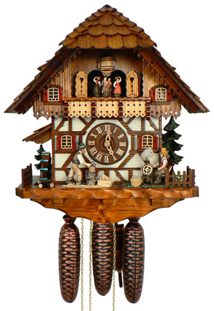 8-Day Black Forest Chalet coocoo clock. The clock is white with timbers, the upper section has light wood. On the left is a water wheel and a tree. A wood chopper chops wood, on the right, a woman spins yarn, a wicker basket is holding her supplies. There is also a low fence and a green tree on the right. The ornate wide balcony above the dial showcases the dancers, above them sits the cuckoo door. The four windows have red shutters and the roof has shingles.