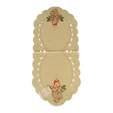 Oval cream color table linen with scalloped edges. On either end is a design of a lighted red candle, decorated with flowers and holly leaves, while cutouts run the length of the linen.