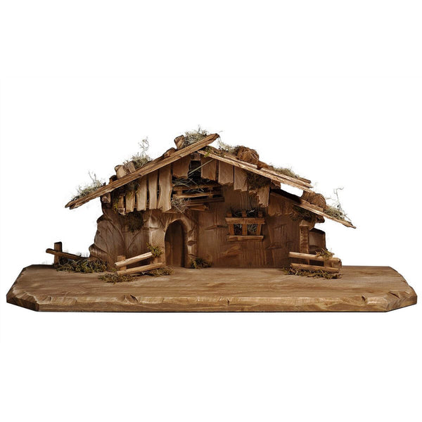 The wooden stable made of Sycamore maple features a roughly hewn base for the figurines of the nativity set. There are split-rail fence sections on both sides of the stable and a third fence sits on the back left corner. A rounded door at an angle on the left front leads to the inside of the wooded stable made of sycamore maple. The upper story underneath the roof is a hay storage and covered with boards. The roofline is rather flat and features stones and dried moss. 