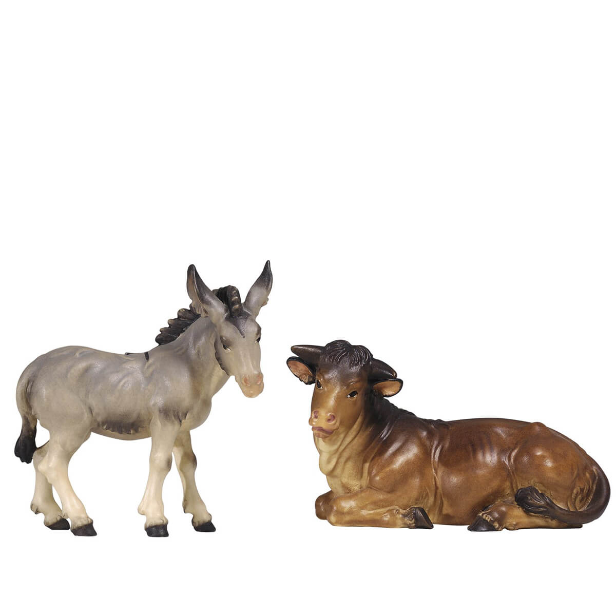 The gray donkey is standing and turns his head slightly to the right. The donkey’s mane is dark. The large brown ox is lying down and has his head turned to the left. Both wooden figurines are carved out of sycamore maple and painted with oil paint.