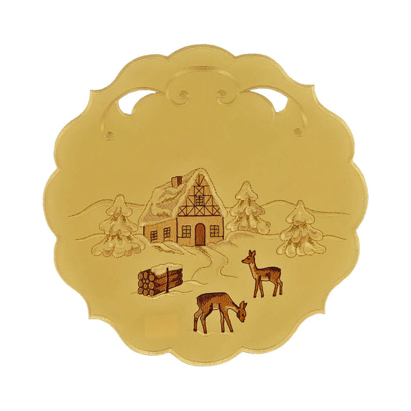 Round cream color table linen with scalloped edges and cutouts, and a design of a snow covered chalet and forest with deer and a bundle of wood.