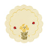 Round white table linen with scalloped edges, an interior yellow border, and a design of primrose flowers and daisies with ladybugs around it.