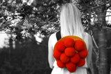 A blond Black Forest beauty wearing a traditional red Bollenhut on her back, standing in a black-and-white Black Forest.