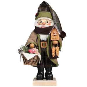 Ulbricht Santa Nutcracker in beige-green coat with gray patterned pointed hat and scarf in front of the face. He is on his way to the forest to bring presents to his friends. In one hand he holds a basket with pine branches, mushrooms and gifts, in the other a birdhouse in the form of a Cuckoo Clock with weights made of birdseed. 